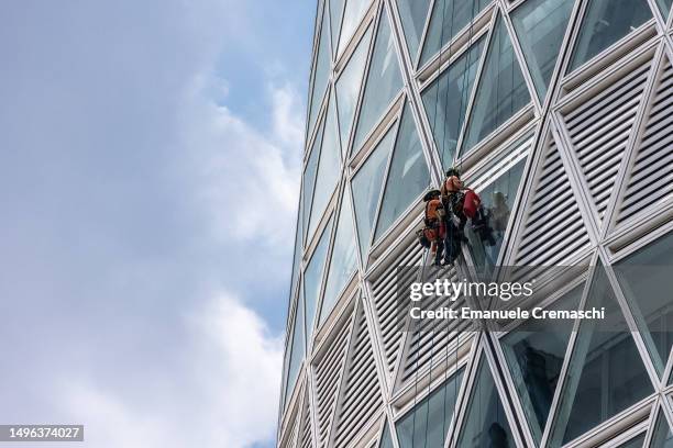 Two building contractors repair and clean a window while abseiling down of the "Nido Verticale" , the new HQ building of UnipolSai insurance group...