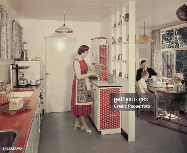 Interior view of a woman preparing drinks for her sons in the kitchen as her husband pours a portion of Shreddies breakfast cereal into his son's...