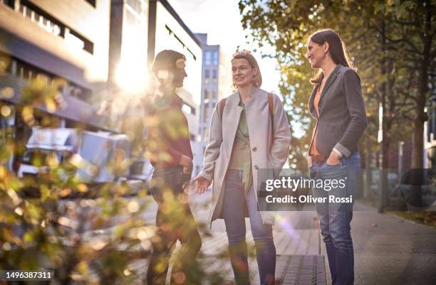 three women talking on sidewalk in the city - gegenlicht stadt stock-fotos und bilder
