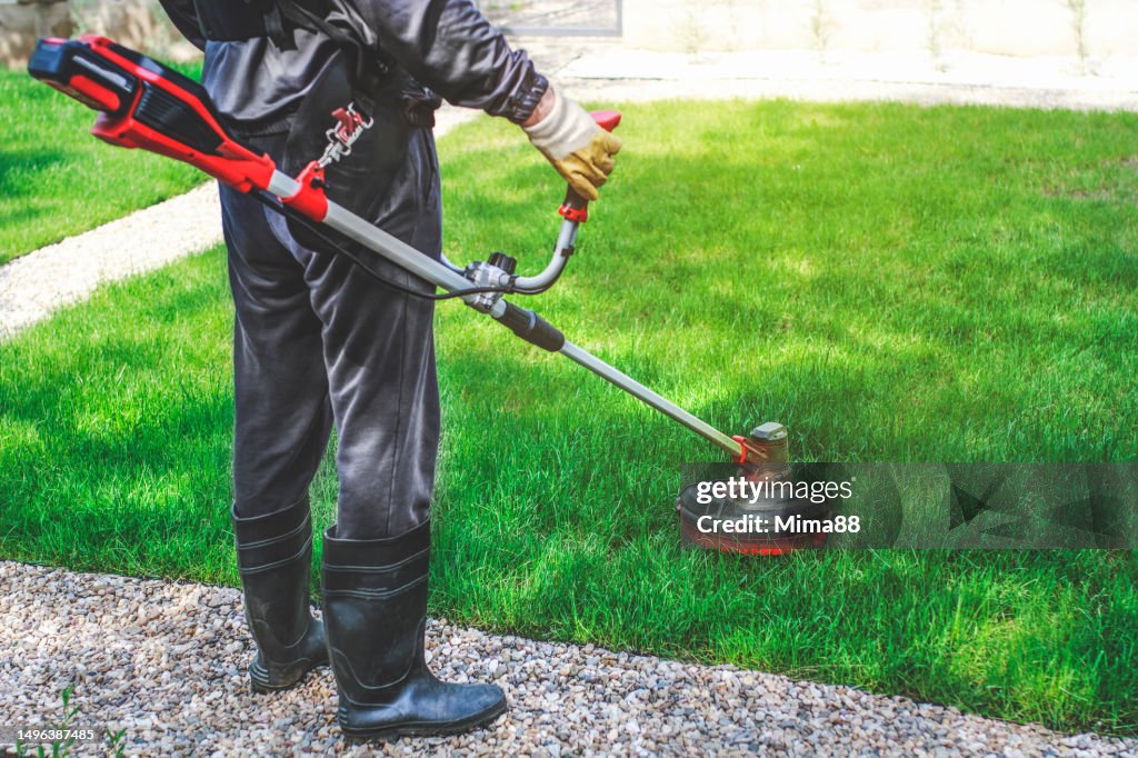 Mann schneidet Gras mit dem Akku-Freischneider im Garten