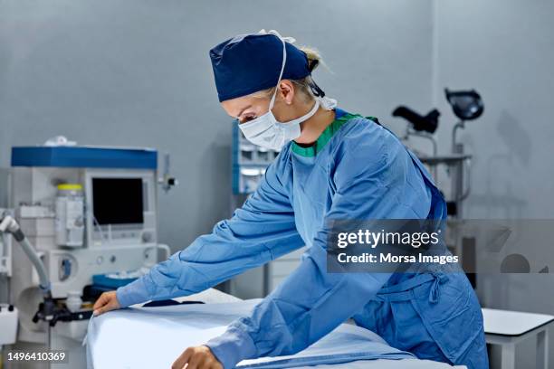 young surgeon preparing bed in operating room - chirurgenkappe stock-fotos und bilder