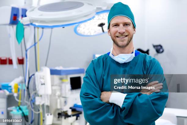 surgeon standing arms crossed in operating room - ropa de operar fotografías e imágenes de stock