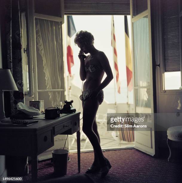 Hotel guest uses the telephone in her room at the Carlton Hotel, Cannes, France, 1958.