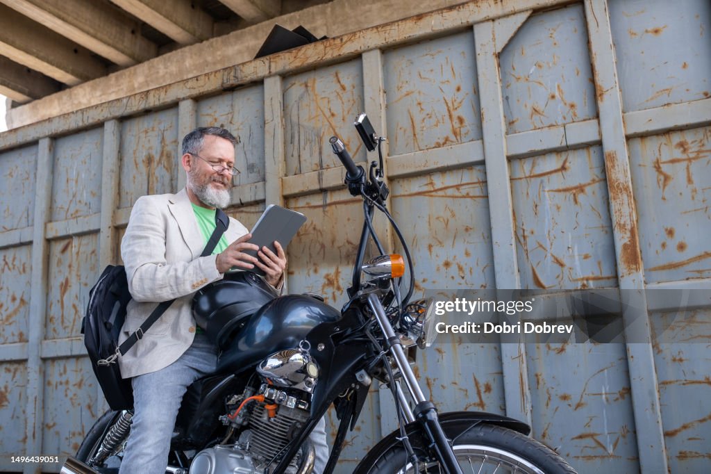 Ein reifer Mann trägt ein hellgrünes T-Shirt, eine beige Jacke und graue Jeans auf einem Bobber-Motorrad.