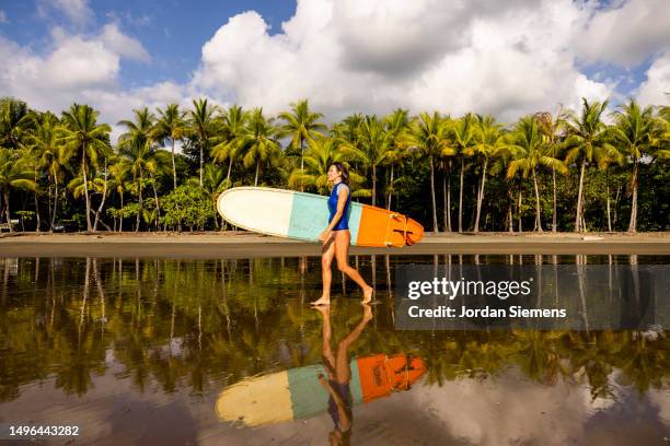 a woman walking with her surboard towads the beach to go surfing. - water sport stock pictures, royalty-free photos & images