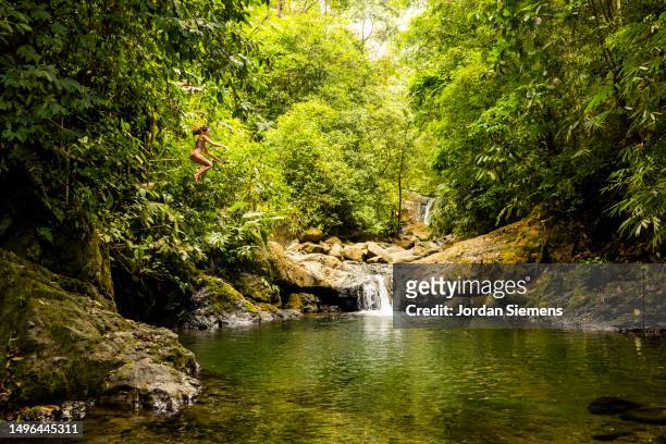 a woman jumping off a cliff into a beautiful pool of water in costa rica - costa rica waterfall stock pictures, royalty-free photos & images