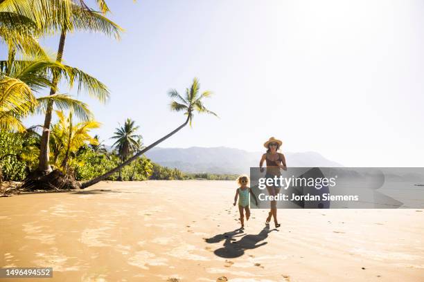 a mother and her daughter running down a palm tree scattered beach in costa rica. - costa rica stockfoto's en -beelden