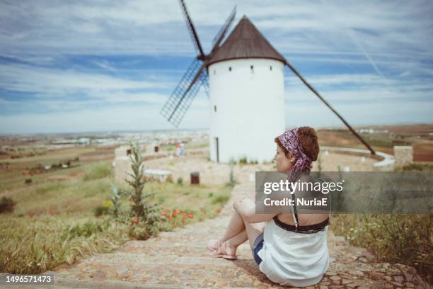 woman sitting in front of a traditional windmill, don quixote's windmills, molinos de viento de consuegra, consuegra, toledo, castilla la mancha, spain - castilië la mancha stockfoto's en -beelden