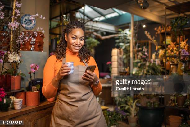 beautiful diverse female florist using handheld technology working in her flower shop - florist bildbanksfoton och bilder