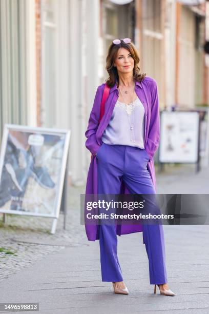 German actress Gerit Kling, wearing a dark purple coat by Seidensticker, dark purple pants by MBYM, a light purple top by Liu Jo, a pink shopping bag...