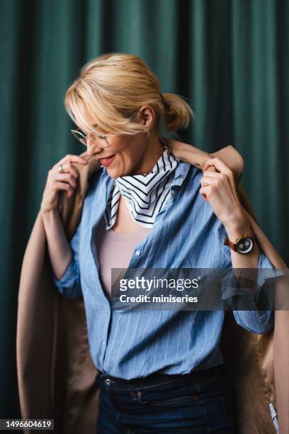 donna d'affari felice che mette su cappotto nel ristorante - businesswoman blond looking left foto e immagini stock