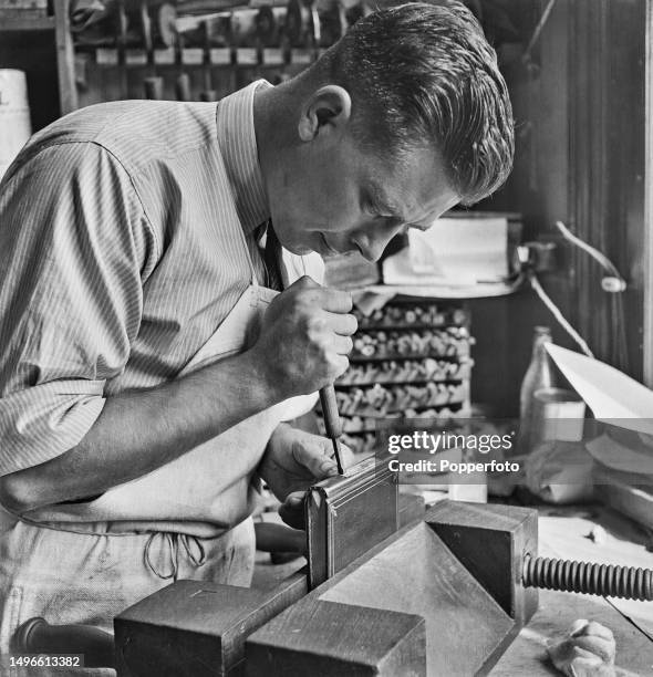 Gold-finisher Albert Machell stamps gold leaf designs onto the spine of a leather bound book held in a vice in the workshop of English bookbinder...