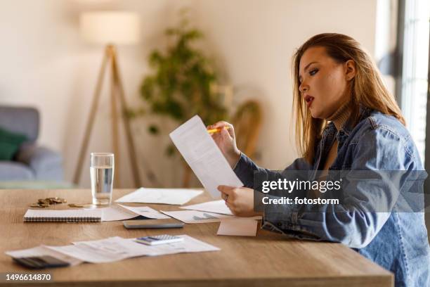 young woman reading values on her financial bill when sorting out home finances - paycheck stock pictures, royalty-free photos & images