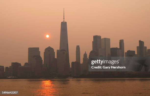 Smoke continues to shroud the sun as it rises behind the skyline of lower Manhattan and One World Trade Center in New York City on June 7 as seen...