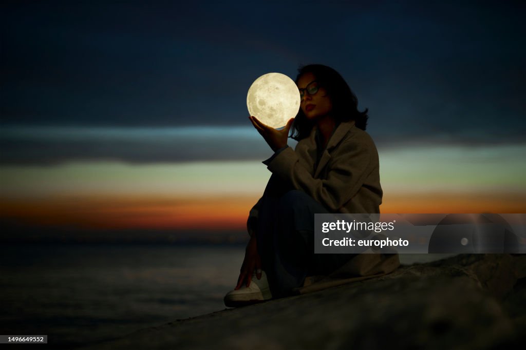 Young lady playing with a moon shaped artificial lamp outdoors