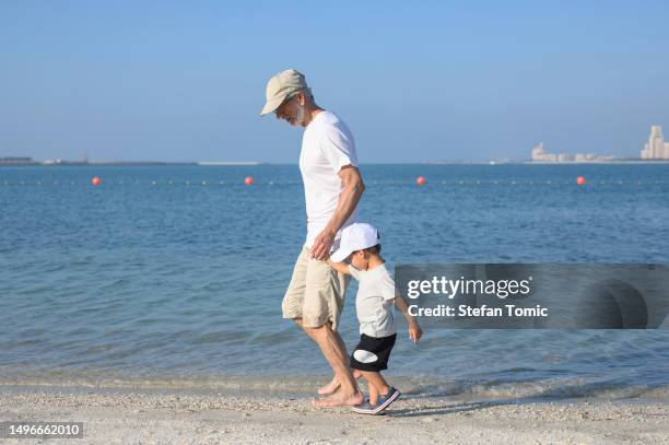 two year old multiracial baby boy and his grandpa walking on the beach - grandson stock pictures, royalty-free photos & images