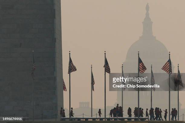 Tourists walk around the base of the Washington Monument as wildfire smoke casts a haze of the U.S. Capitol on the National Mall on June 07, 2023 in...