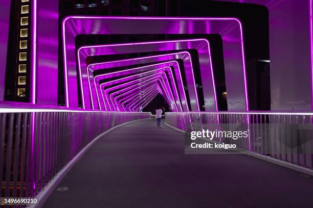 pedestrians crossing a pedestrian bridge with light effects - neon catwalk stock pictures, royalty-free photos & images