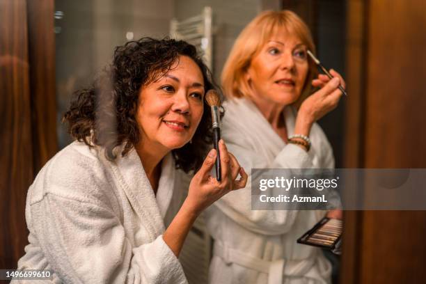 mixed race women getting ready in bathroom - make up brush stockfoto's en -beelden