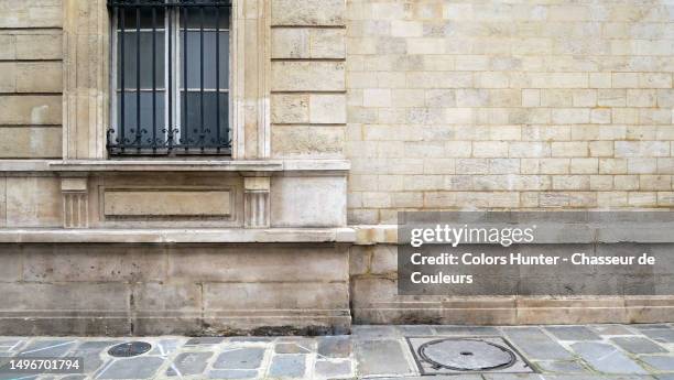 weathered brown stone wall with opaque window and cobblestone sidewalk in paris, france - street wall stockfoto's en -beelden