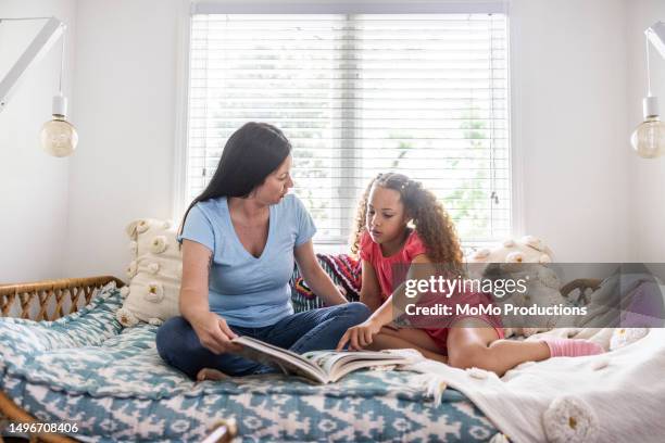 mother reading to daughter on daybed at home - georgia love stock-fotos und bilder