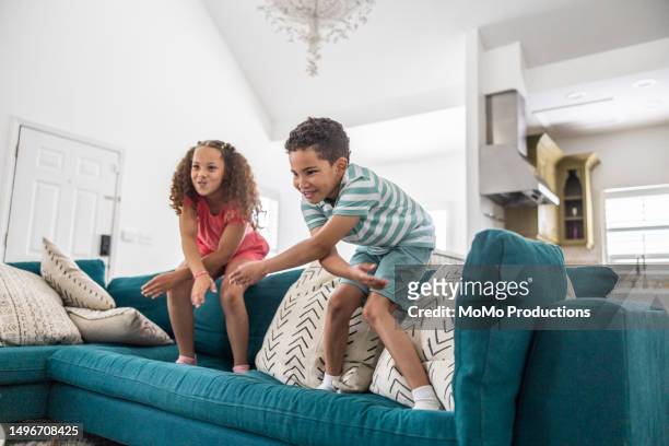 brother and sister jumping on couch at home - jump on sofa stock-fotos und bilder