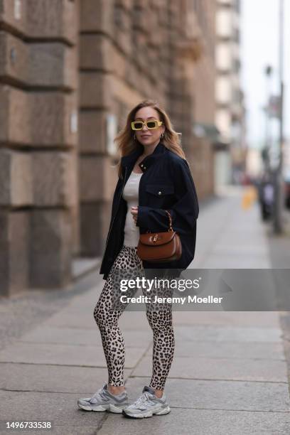 Sonia Lyson wearing Miu Miu navy blue jacket and beige logo Miu Miu top, Gucci Bamboo dark brown leather bag, Loewe yellow shades, New Balance beige...