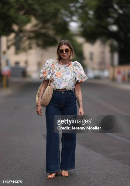 Aline Kaplan wearing Baum & Pferdgarten wide leg blue denim pants, & other stories white flower pattern cropped blouse and orange summer heels and...