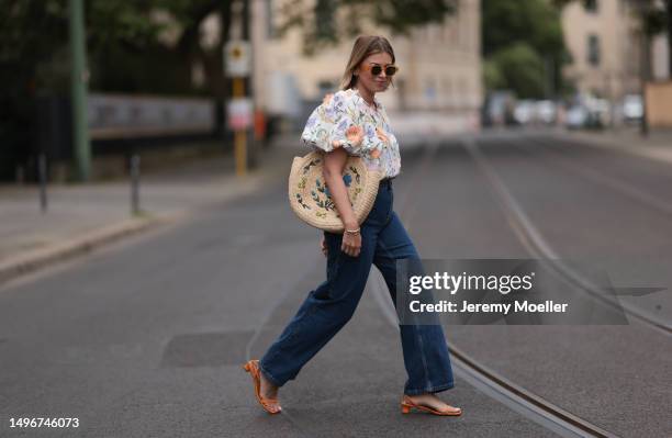 Aline Kaplan wearing Baum & Pferdgarten wide leg blue denim pants, & other stories white flower pattern cropped blouse and orange summer heels and...