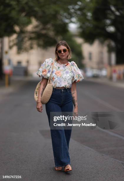 Aline Kaplan wearing Baum & Pferdgarten wide leg blue denim pants, & other stories white flower pattern cropped blouse and orange summer heels and...