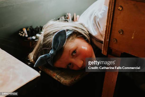 a shy little girl lies on her front, flicking her eyes up towards the camera, with a serious expression. - hair bow stock pictures, royalty-free photos & images