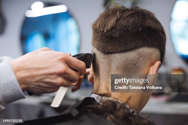 teenage boy sitting in hair salon while hairstylist cutting his hair using trimmer - shaved head stock pictures, royalty-free photos & images