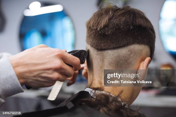 teenage boy sitting in hair salon while hairstylist cutting his hair using trimmer - ruffled hair stock pictures, royalty-free photos & images