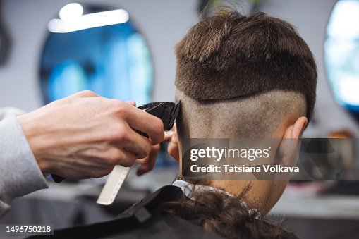 Teenage boy sitting in hair salon while hairstylist cutting his hair using trimmer Teenage boy sitting in hair salon while hairstylist cutting his hair using trimmer
