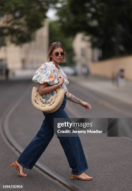 Aline Kaplan wearing Baum & Pferdgarten wide leg blue denim pants, & other stories white flower pattern cropped blouse and orange summer heels and...