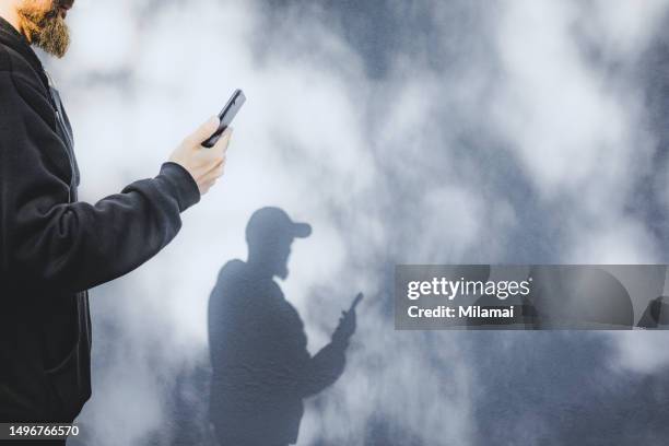 shadow of person with smart phone and cap - acosador fotografías e imágenes de stock