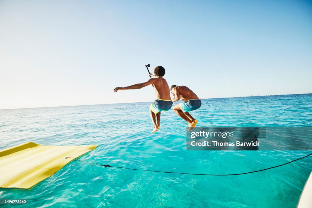 Wide shot brothers jumping into ocean with action camera from yacht