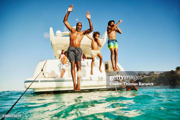 wide shot father and sons jumping into water from swim deck of yacht - mezzo di trasporto marittimo foto e immagini stock
