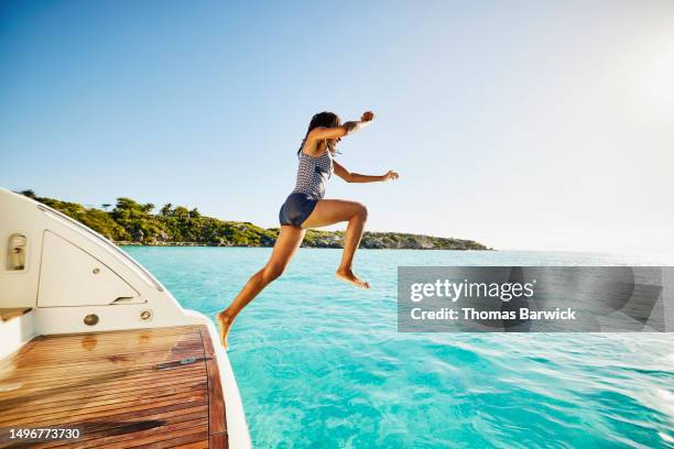 wide shot of teenage girl jumping off swim step of yacht into ocean - jumping of boat photos et images de collection