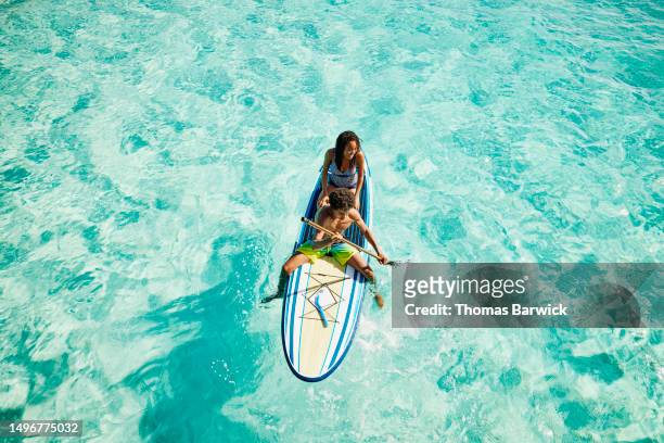wide shot of teenage siblings paddling paddleboard in ocean - travel fotografías e imágenes de stock