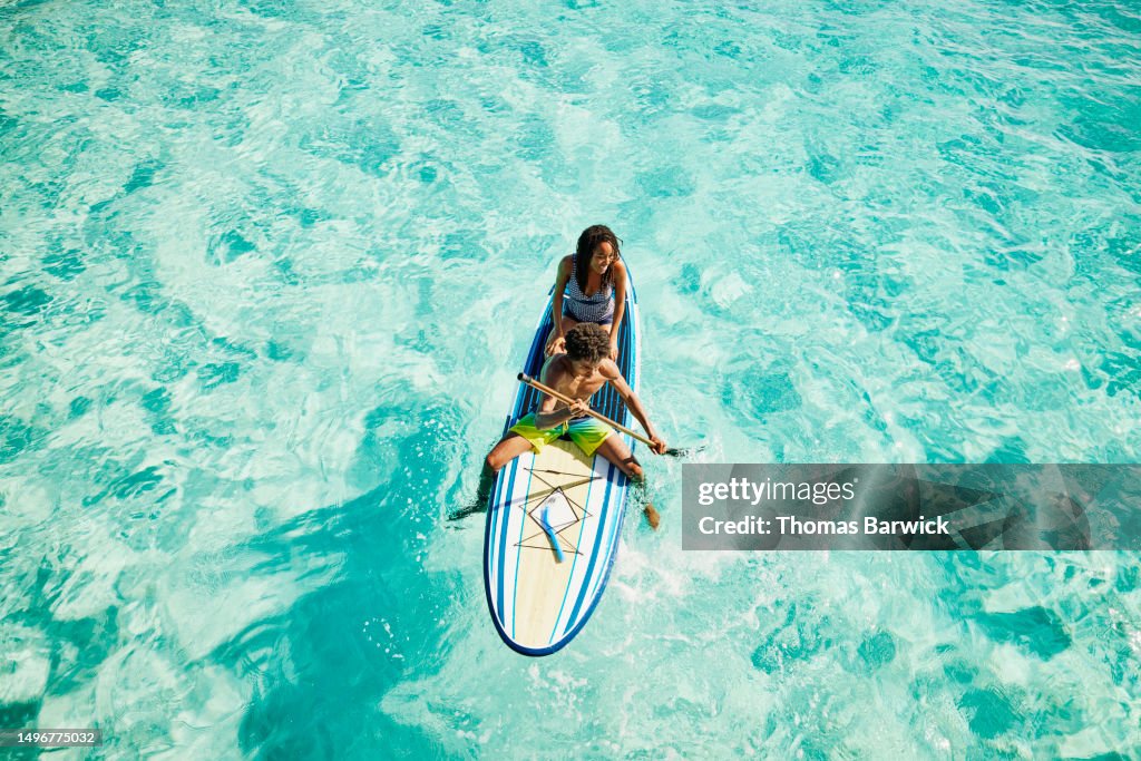 Wide shot of teenage siblings paddling paddleboard in ocean
