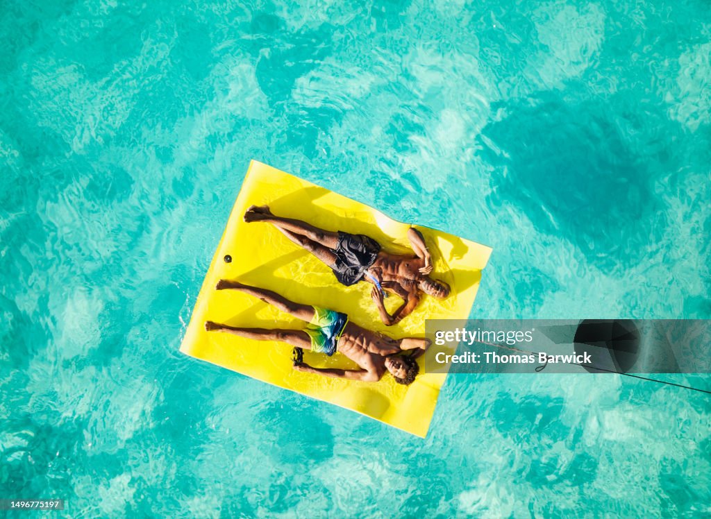 Wide shot of father and son relaxing on swim float in ocean