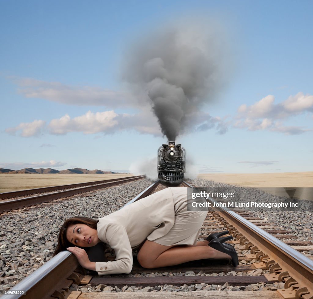 Mixed race businesswoman kneeling on railroad tracks