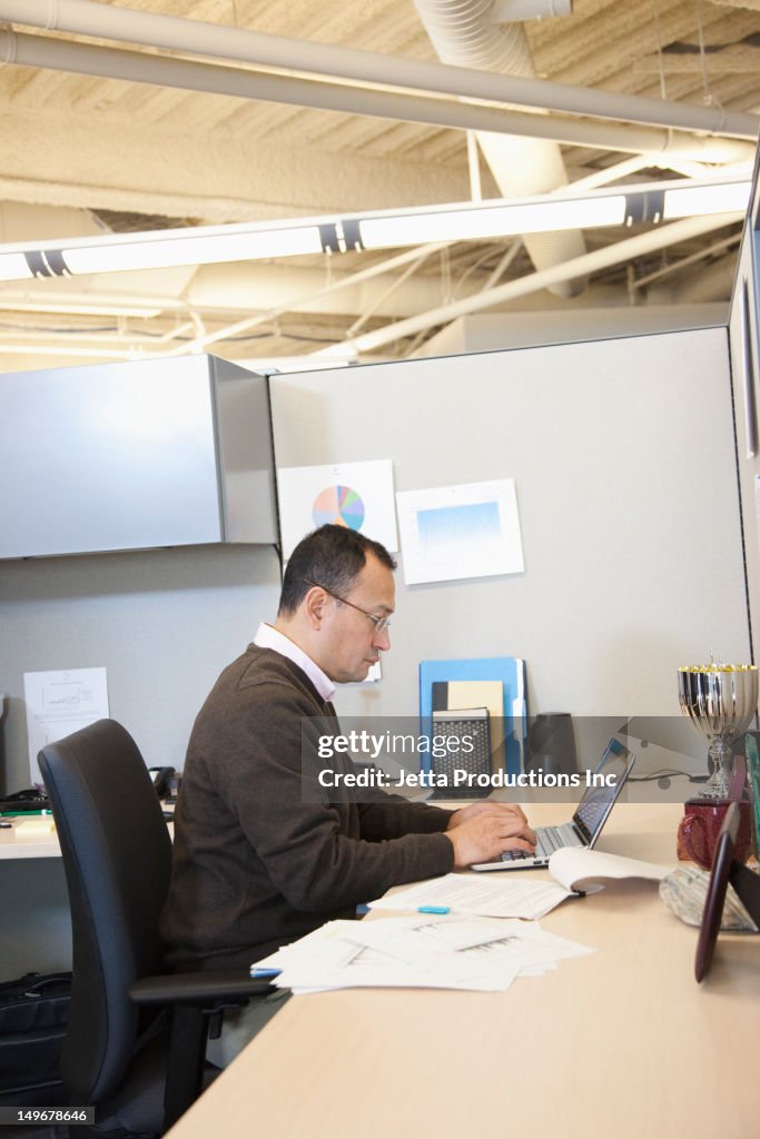 Hispanic businessman working at desk in cubicle