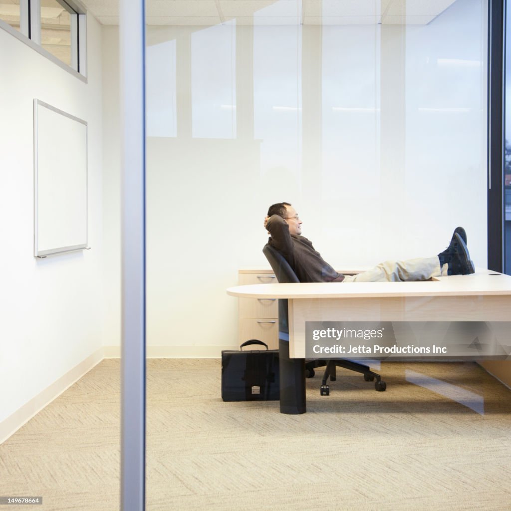 Hispanic businessman sitting on desk with feet up