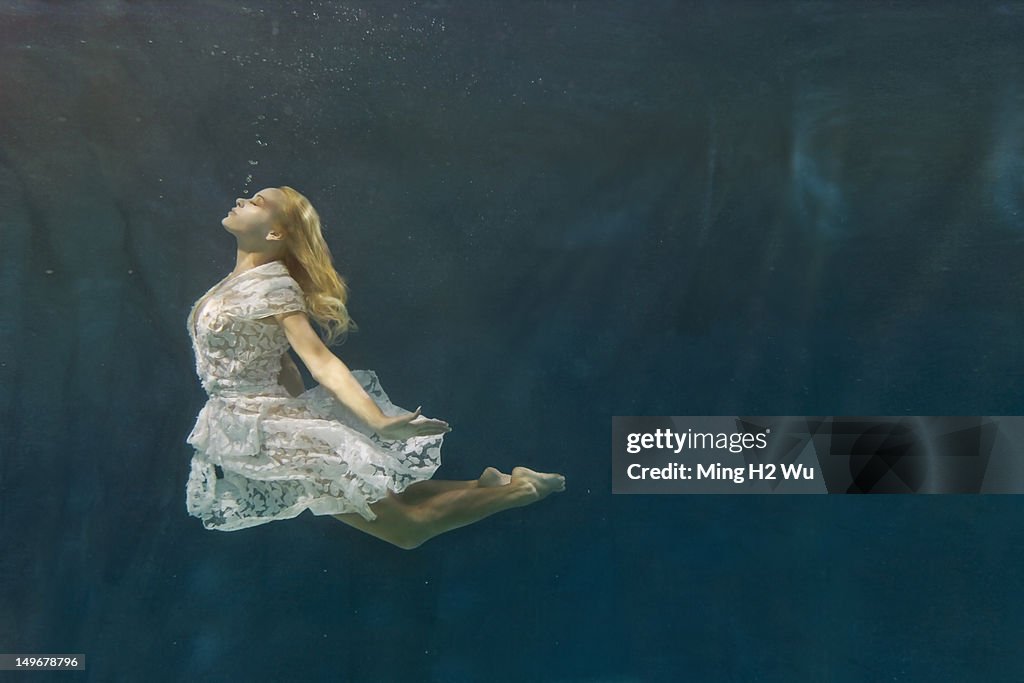 Caucasian woman in dress swimming under water