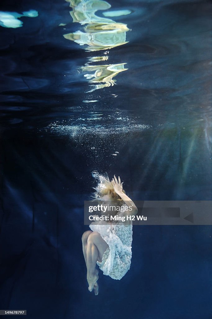 Caucasian woman in dress swimming under water