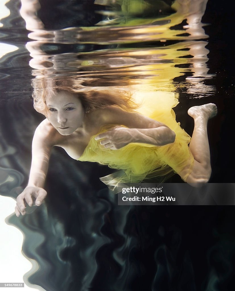 Caucasian woman in dress swimming under water