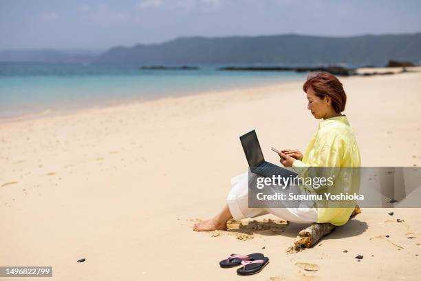 a woman using a laptop on a beach on vacation. - 鹿児島県 fotografías e imágenes de stock