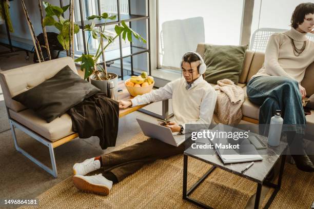 high angle view of programmer using mobile phone sitting with laptop on carpet in creative office - carpet icon stock pictures, royalty-free photos & images